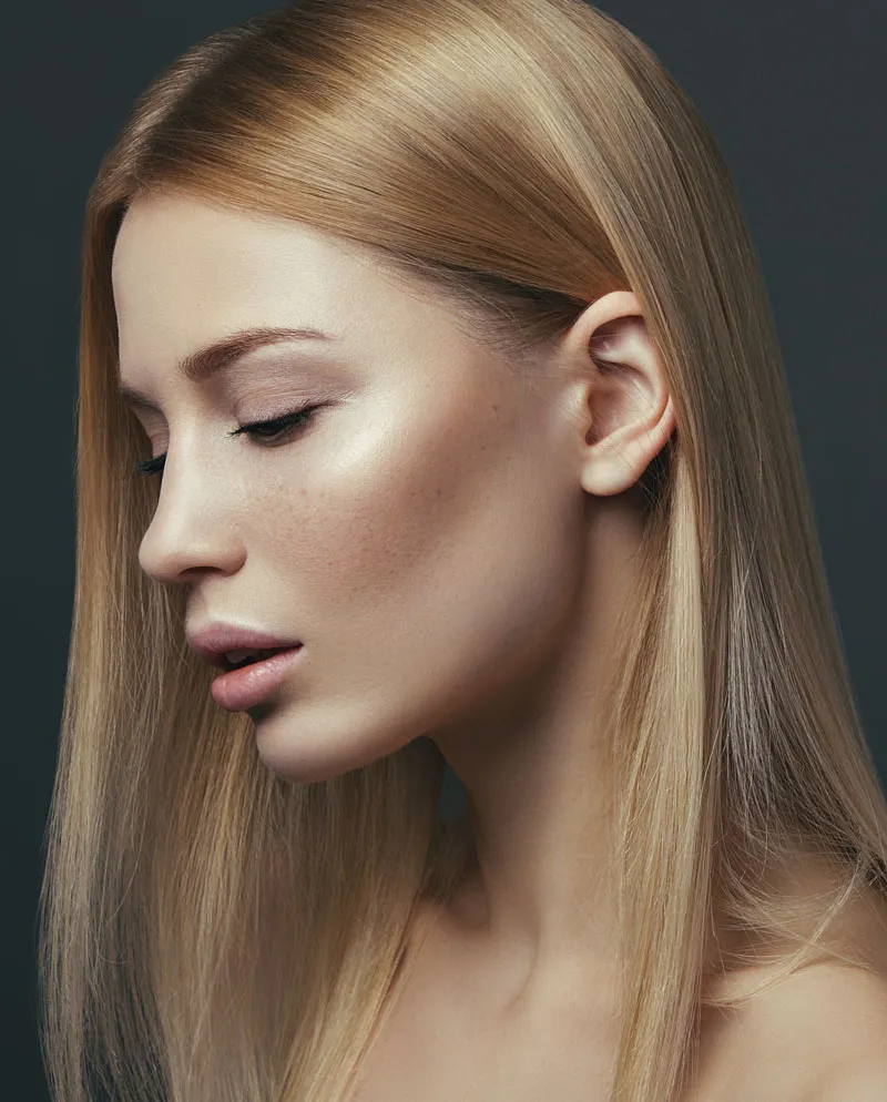 blonde woman with hair behind her ear looking over shoulder