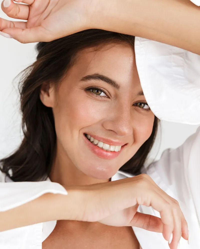 woman in white shirt with arms above head and under chin smiling