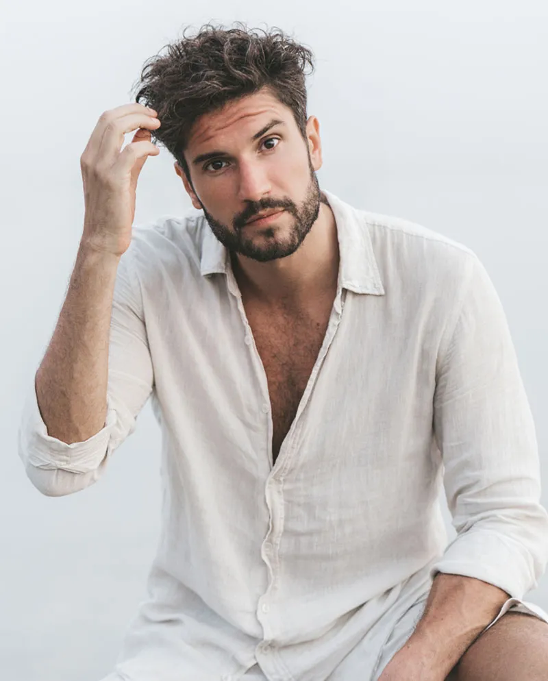 brunette man with beard playing with hair in linen shirt