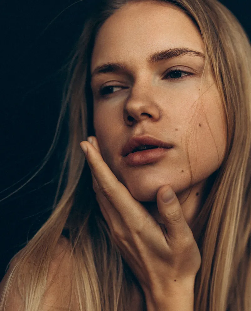 blonde woman with hand under chin looking off into the distance