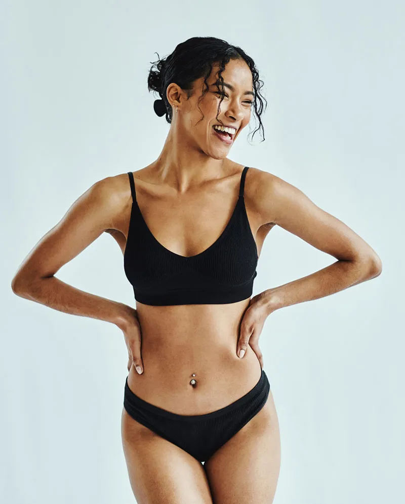 woman in black bra and underwear with hands on hips smiling to the side