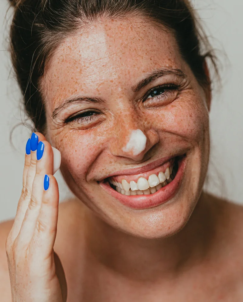 A woman with dabs of lotion on nose and a dolop in hand