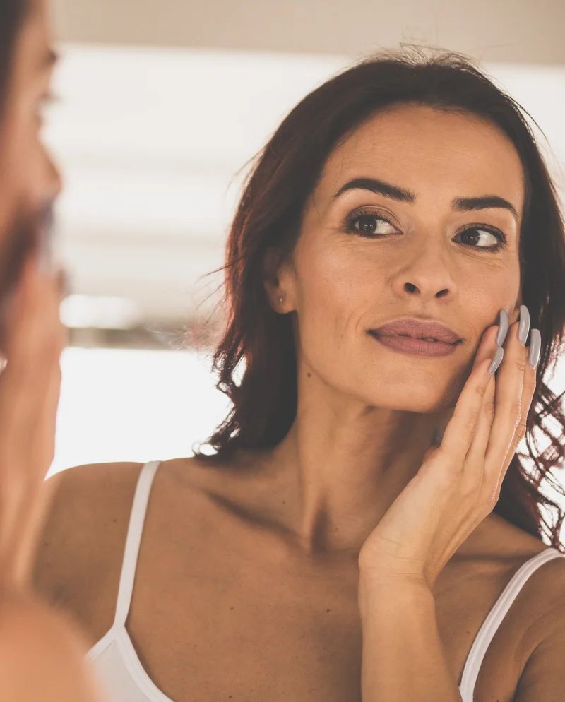 woman touching face while looking into mirror